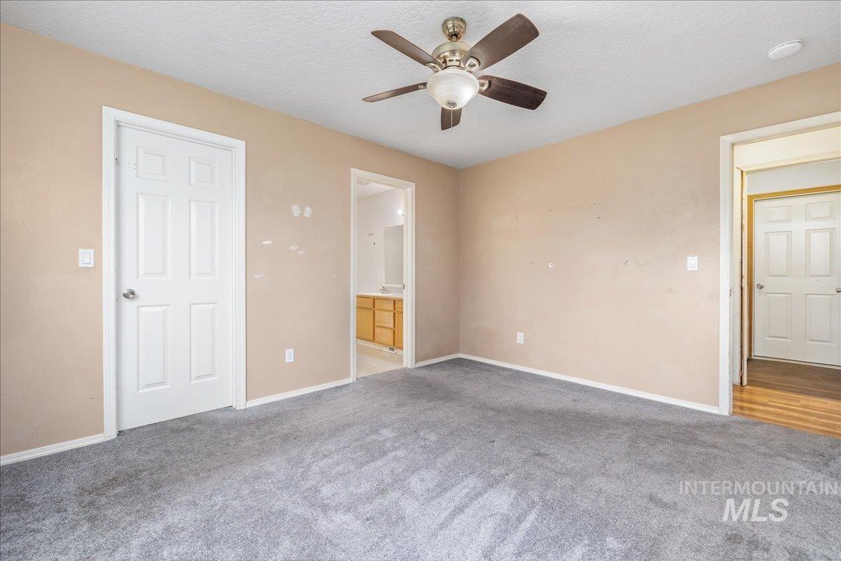 Unfurnished bedroom with ensuite bath, carpet flooring, a textured ceiling, and ceiling fan