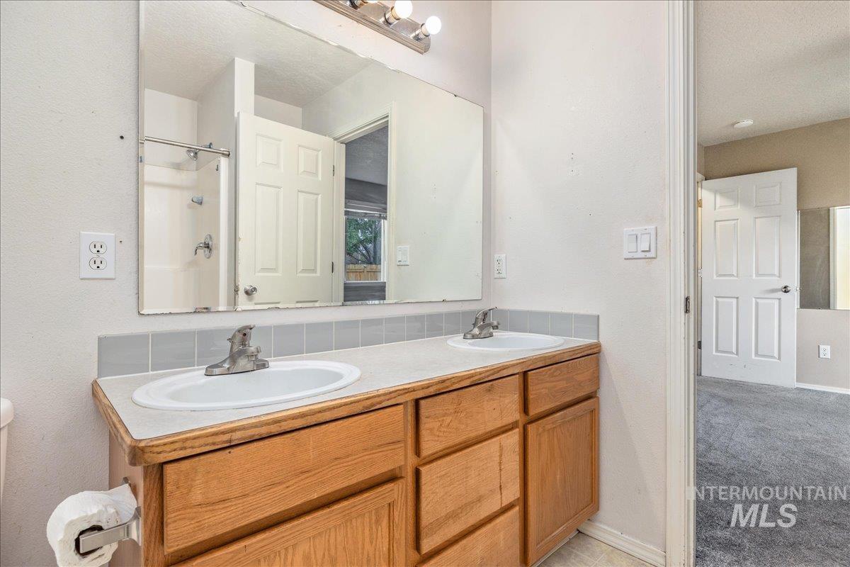 Bathroom with a shower, double vanity, a textured ceiling, a textured wall, and light carpet