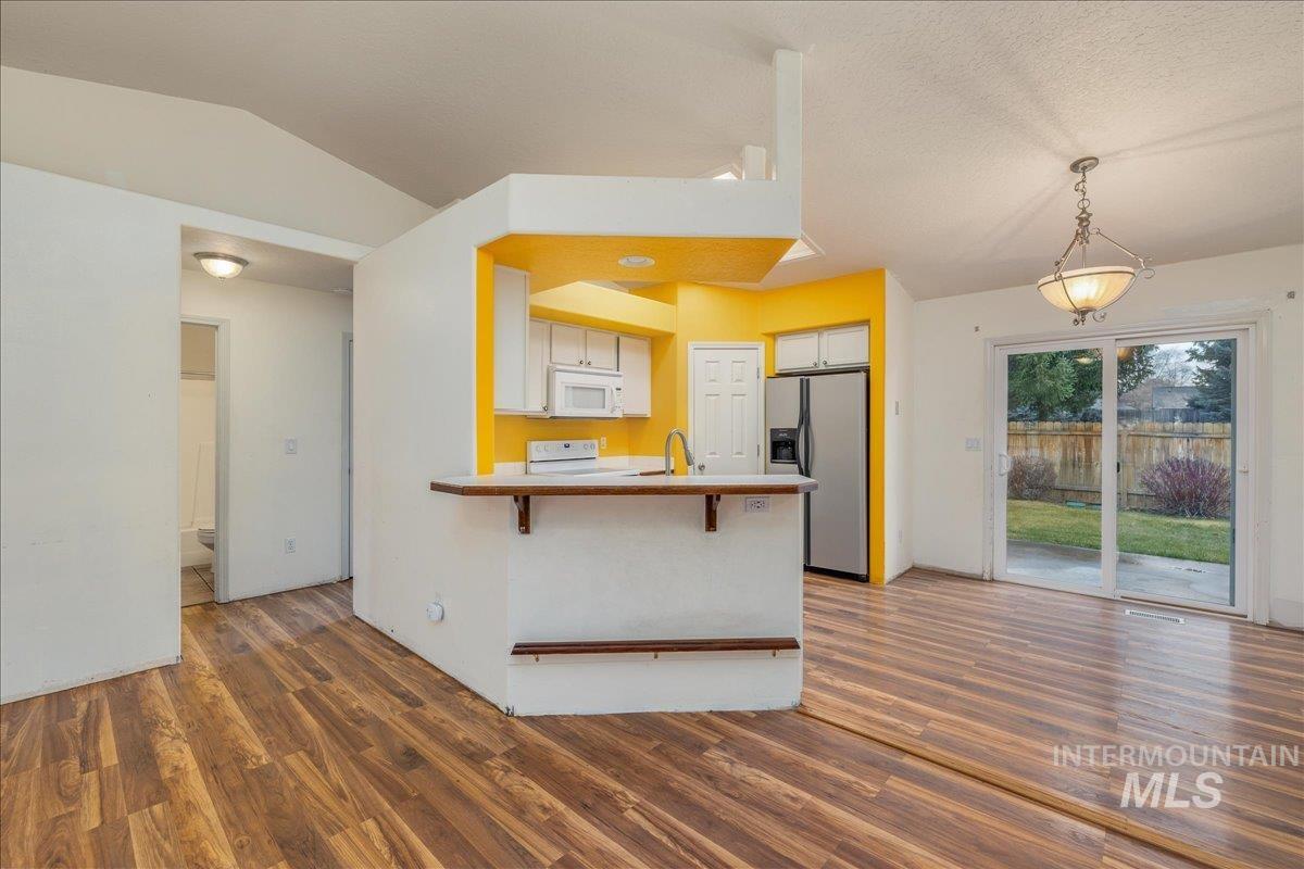 Kitchen featuring a kitchen breakfast bar, white appliances, light countertops, dark wood finished floors, and a peninsula