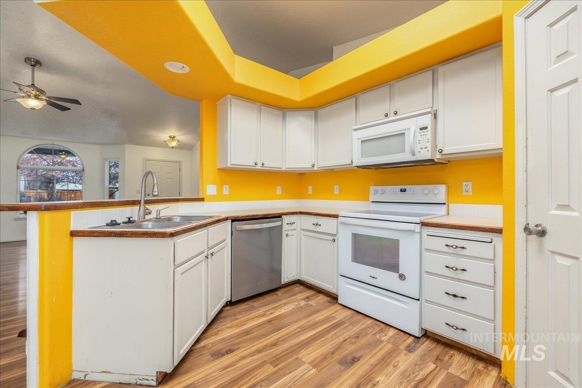 Kitchen featuring white cabinetry, white appliances, light wood-style flooring, and a peninsula