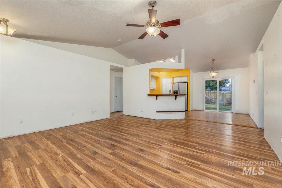 Unfurnished living room with lofted ceiling, wood finished floors, a ceiling fan, and a textured ceiling