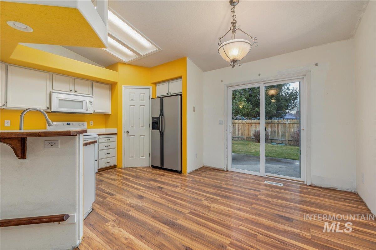 Kitchen with stainless steel fridge, white cabinets, hanging light fixtures, white microwave, and dark wood-style floors