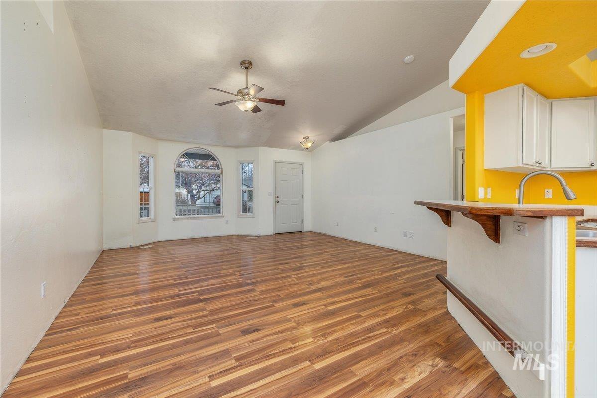 Unfurnished living room featuring vaulted ceiling, light wood-style floors, and a ceiling fan