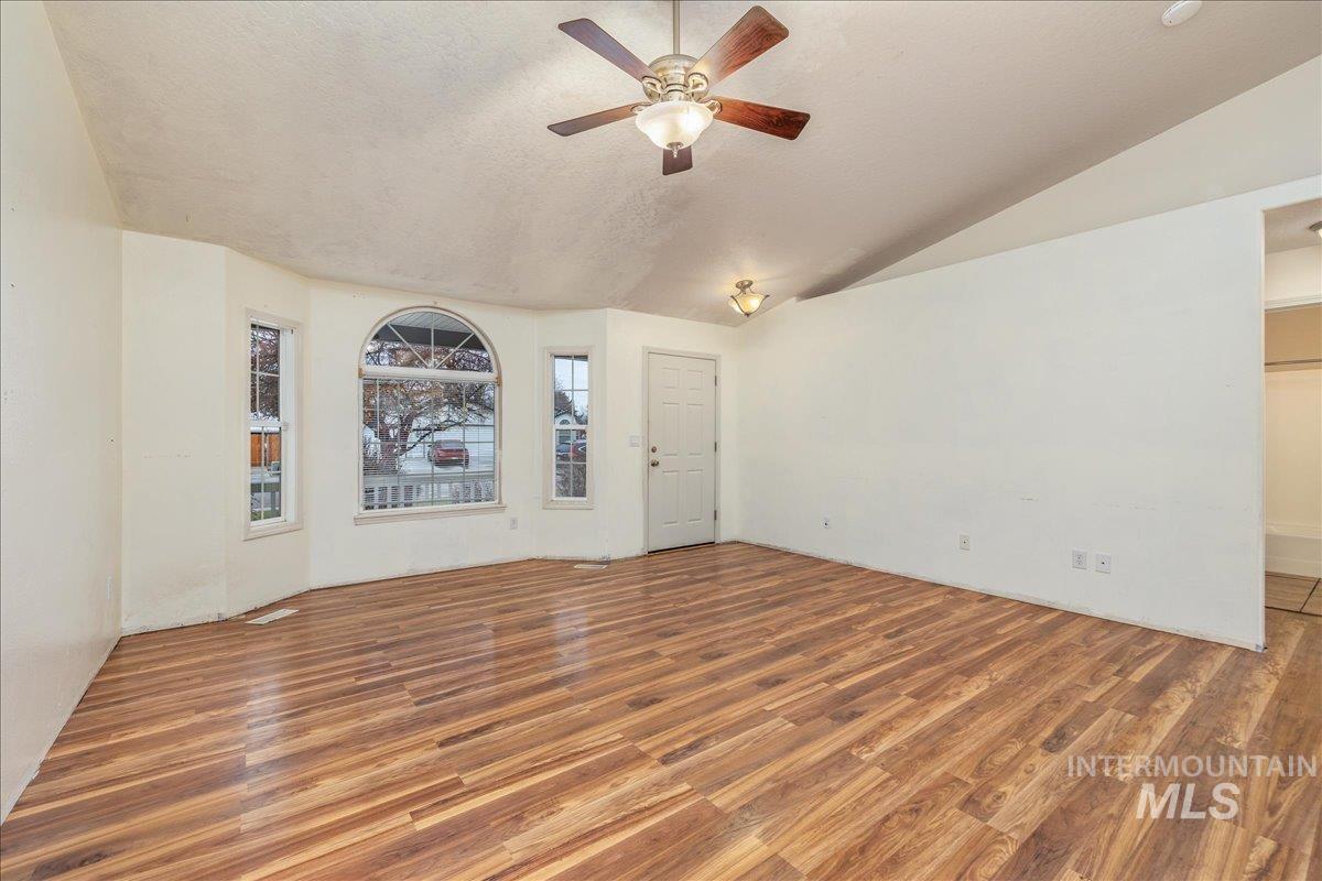 Unfurnished living room featuring vaulted ceiling, wood finished floors, a textured ceiling, and a ceiling fan