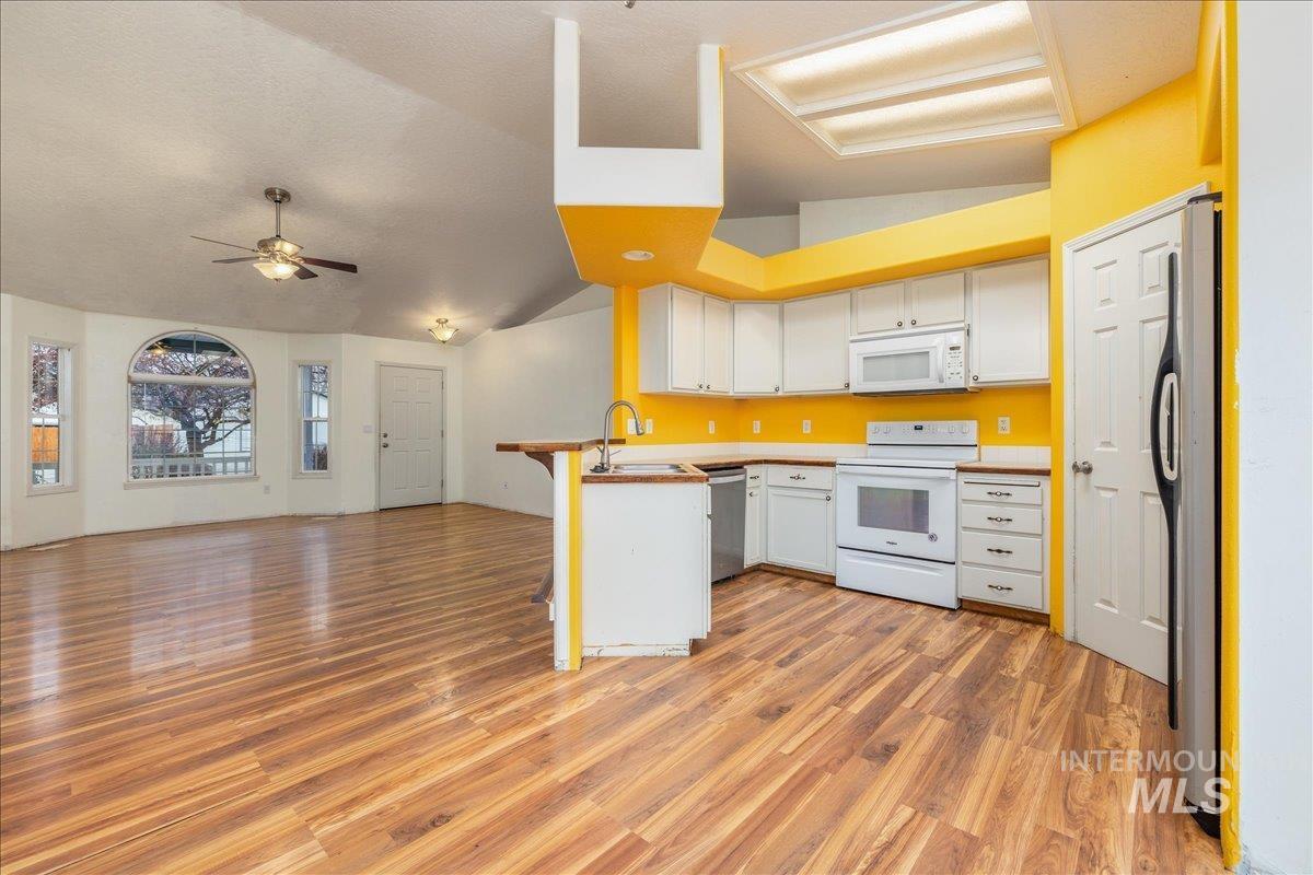 Kitchen featuring open floor plan, vaulted ceiling, white appliances, white cabinetry.