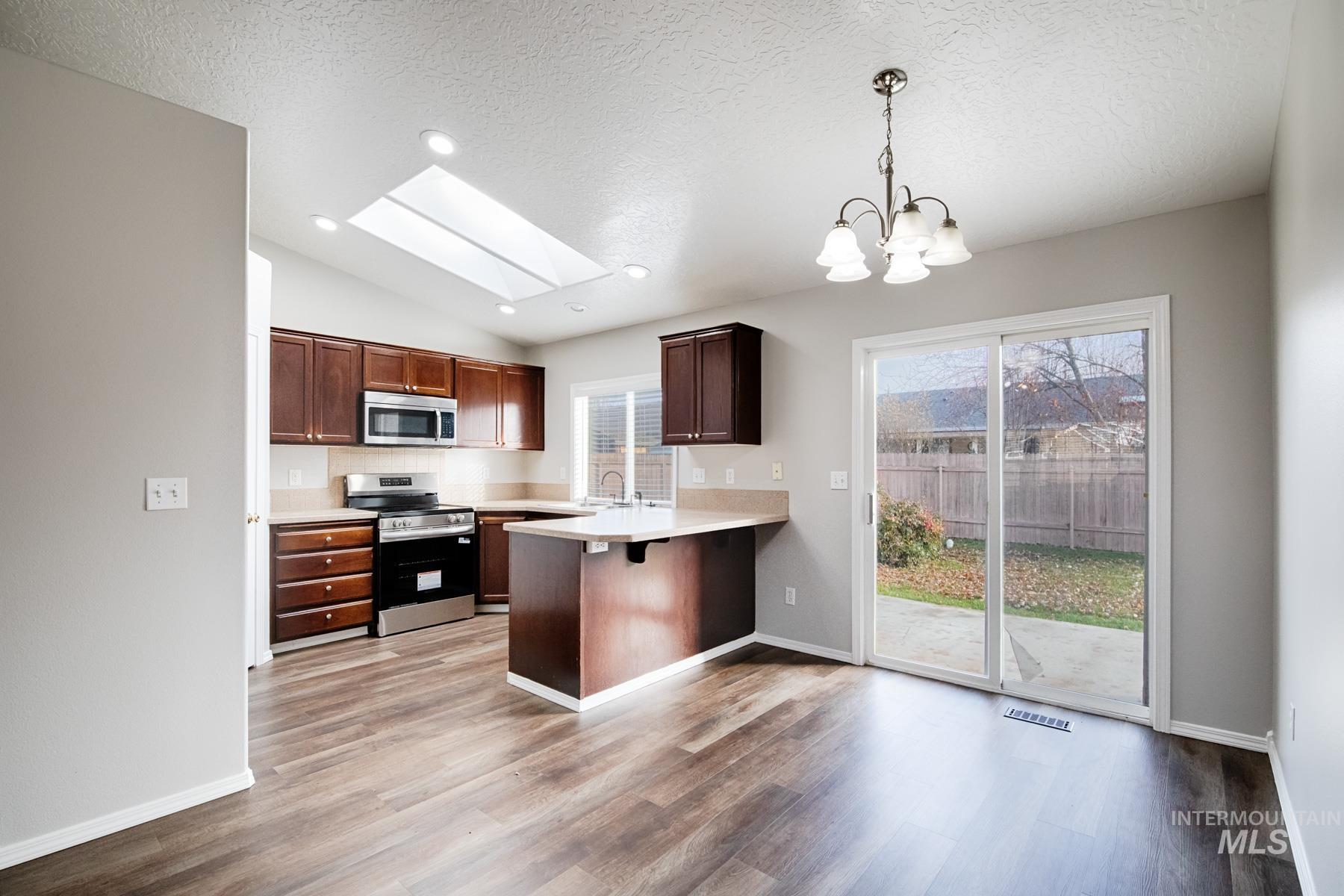 Kitchen featuring a skylight, light countertops, appliances with stainless steel finishes, pendant lighting, and a peninsula