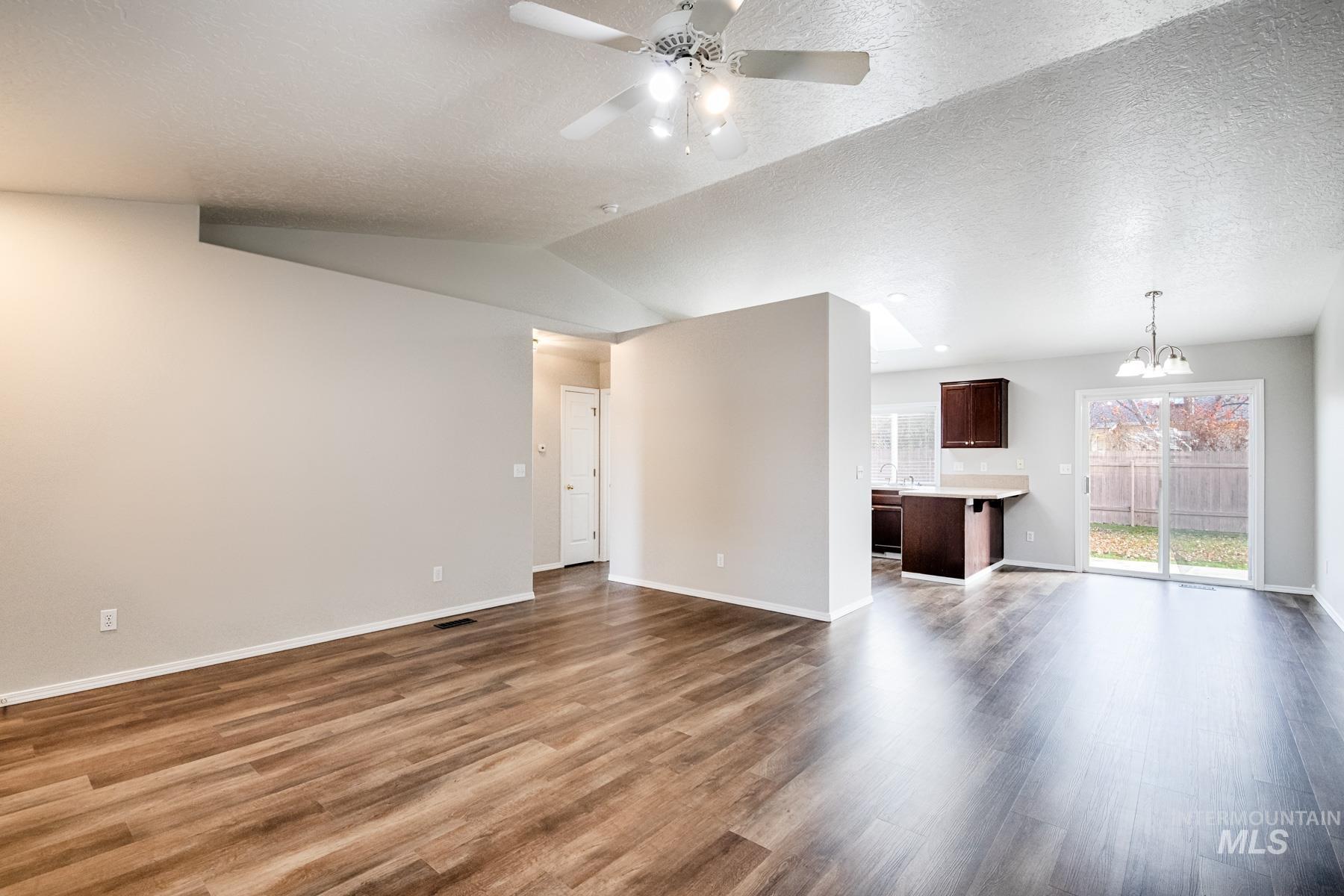 Unfurnished living room with a chandelier, a ceiling fan, a textured ceiling, dark wood finished floors, and vaulted ceiling