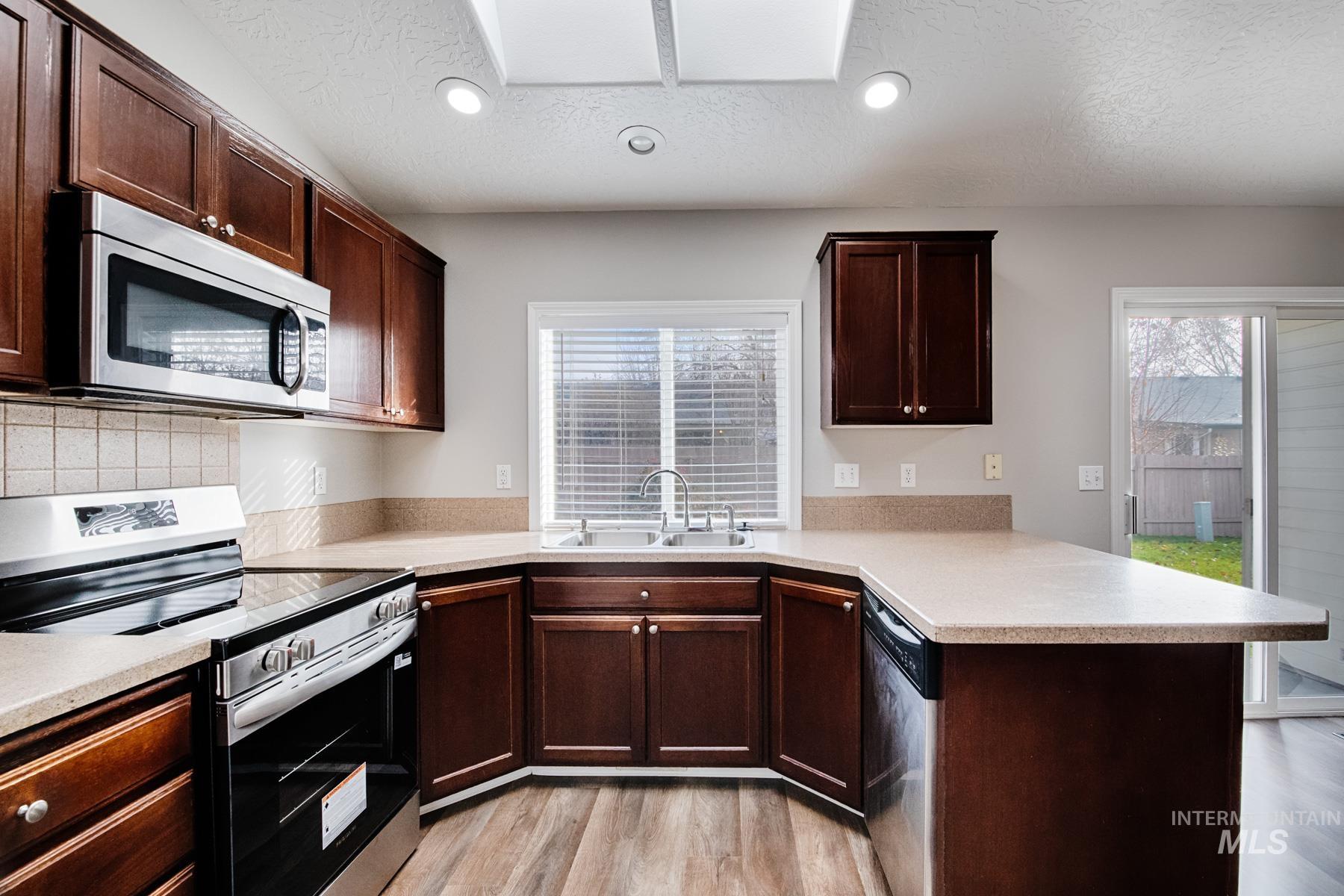 Kitchen with stainless steel appliances, dark brown cabinetry, a peninsula, recessed lighting, and a skylight
