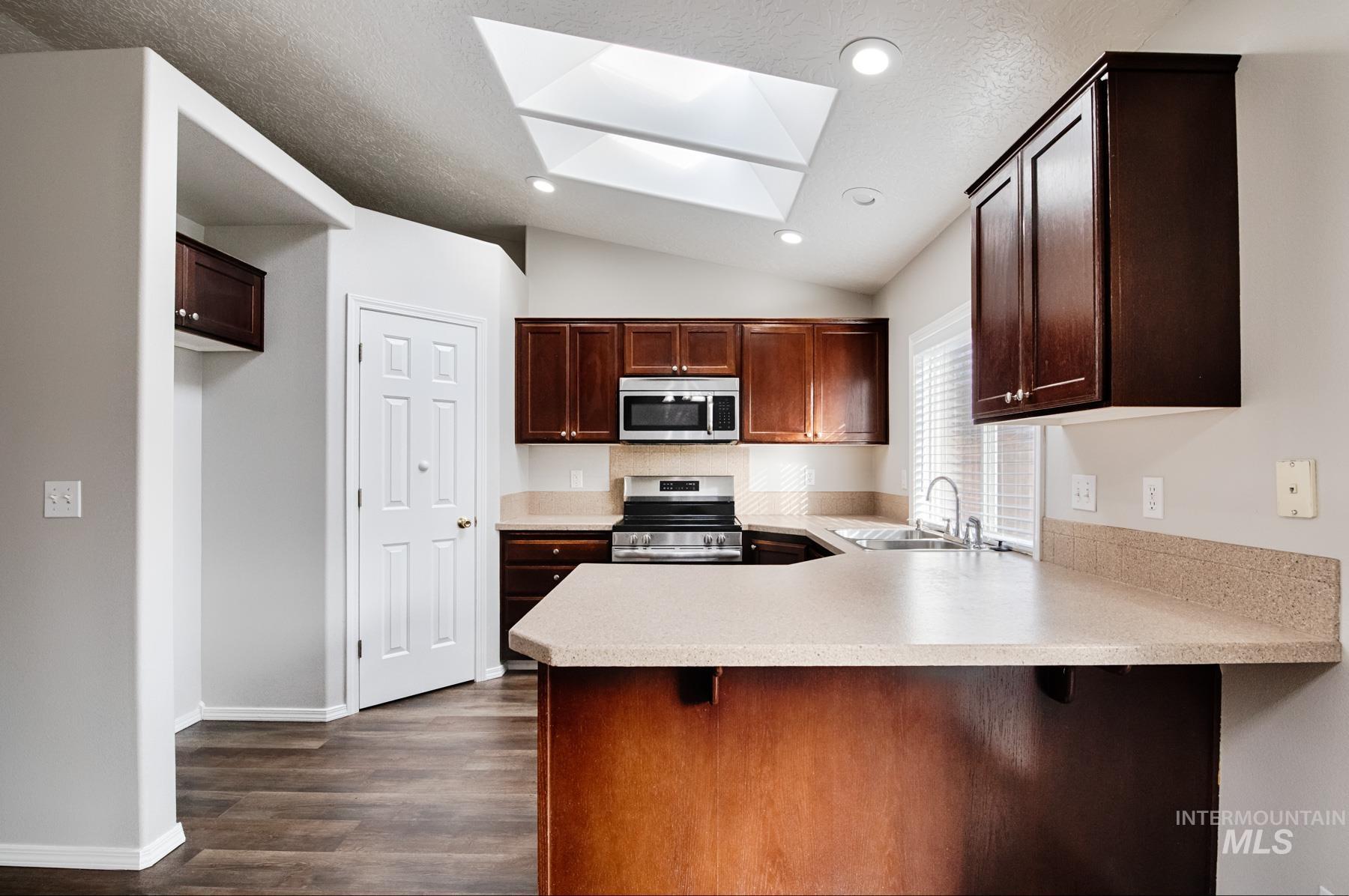 Kitchen with a skylight, a peninsula, light countertops, appliances with stainless steel finishes, and vaulted ceiling