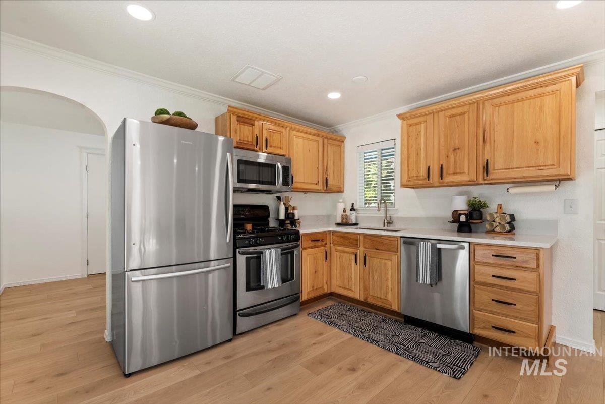Kitchen with stainless steel appliances, light wood-style floors, ornamental molding, recessed lighting, and arched walkways