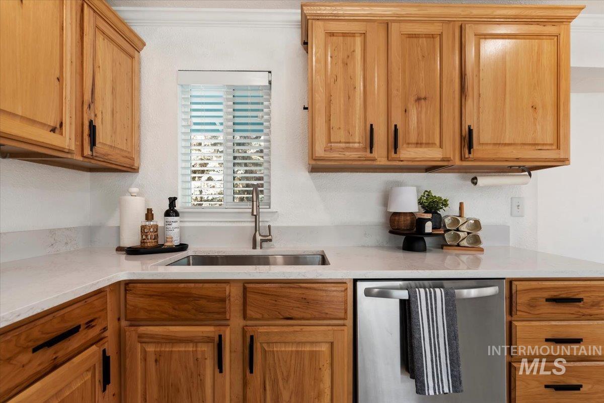 Kitchen featuring stainless steel dishwasher, light stone counters, ornamental molding, and brown cabinets