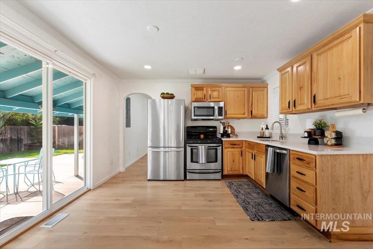 Kitchen featuring arched walkways, appliances with stainless steel finishes, light wood-type flooring, recessed lighting, and crown molding
