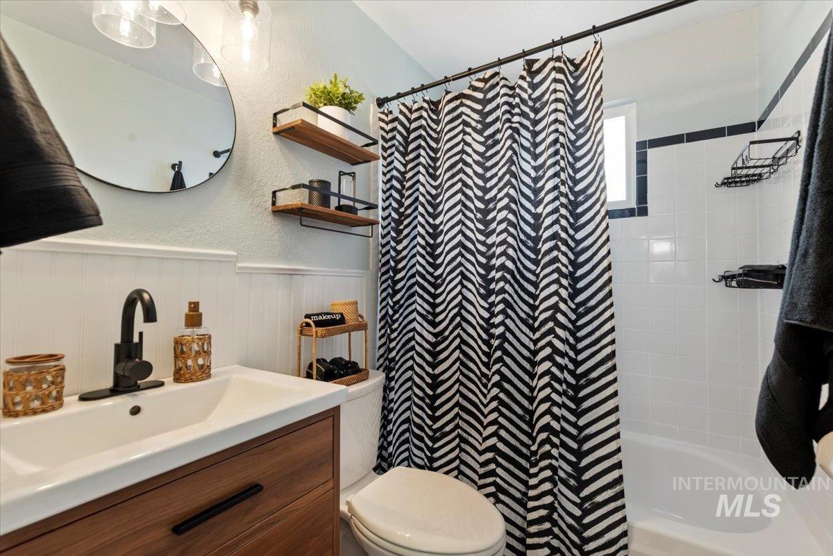 Full bathroom featuring a textured wall, shower / bath combo with shower curtain, and vanity