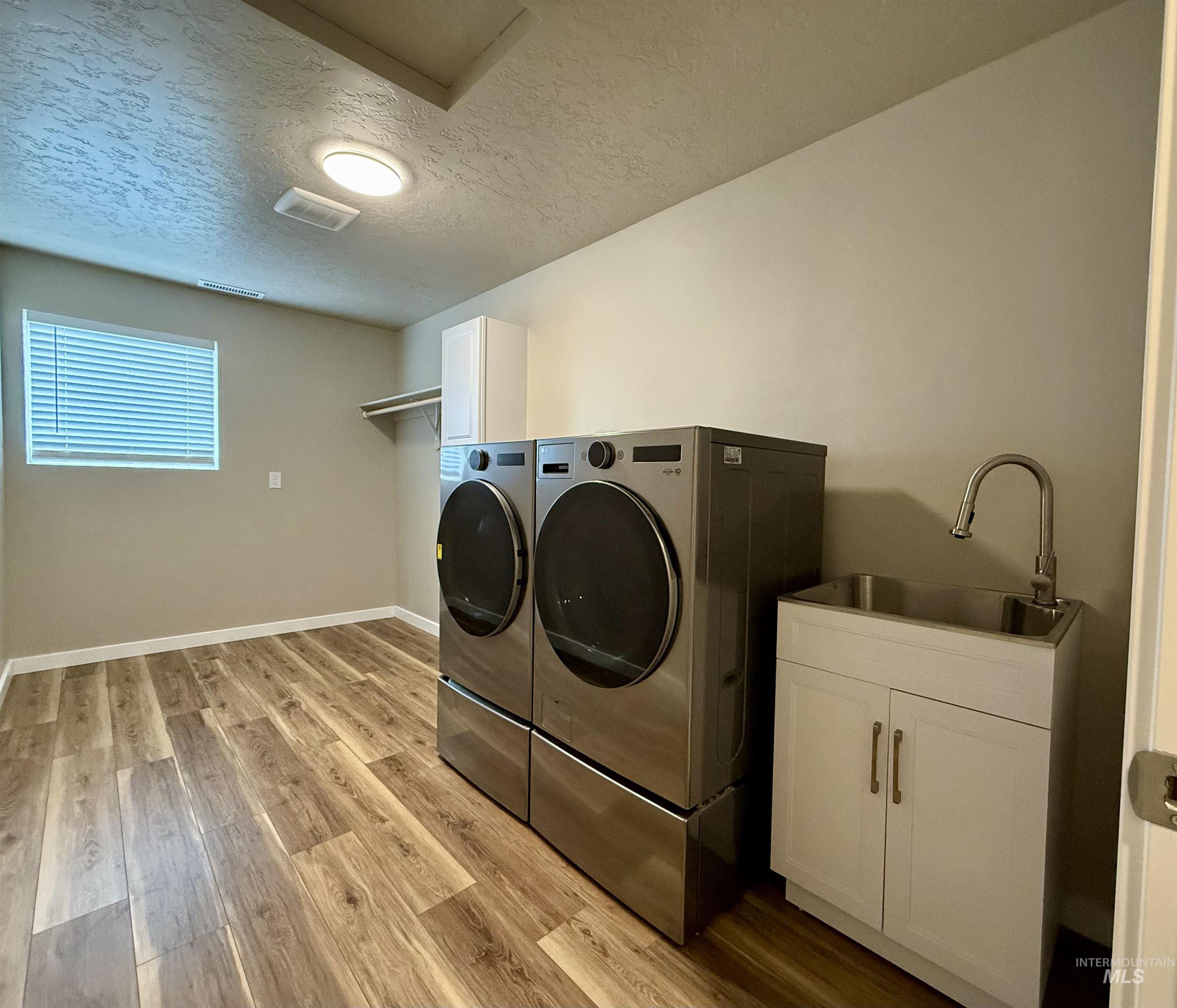Laundry room featuring cabinet space, a textured ceiling, light wood finished floors, and washing machine and clothes dryer