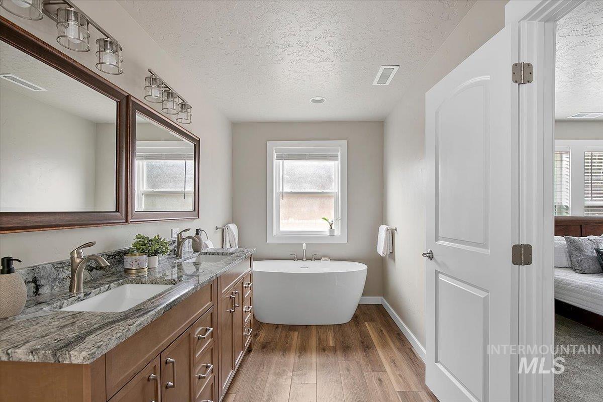 Ensuite bathroom with a freestanding tub, wood finished floors, and double vanity
