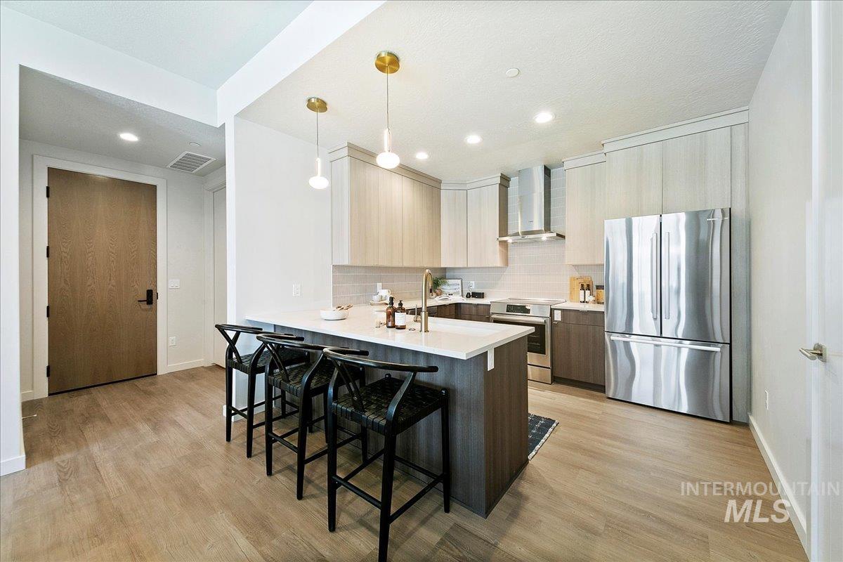 Kitchen featuring stainless steel appliances, decorative light fixtures, a kitchen bar, a peninsula, and wall chimney exhaust hood