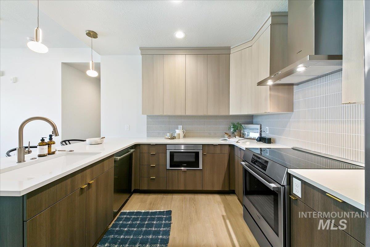 Kitchen featuring wall chimney range hood, appliances with stainless steel finishes, hanging light fixtures, and modern cabinets