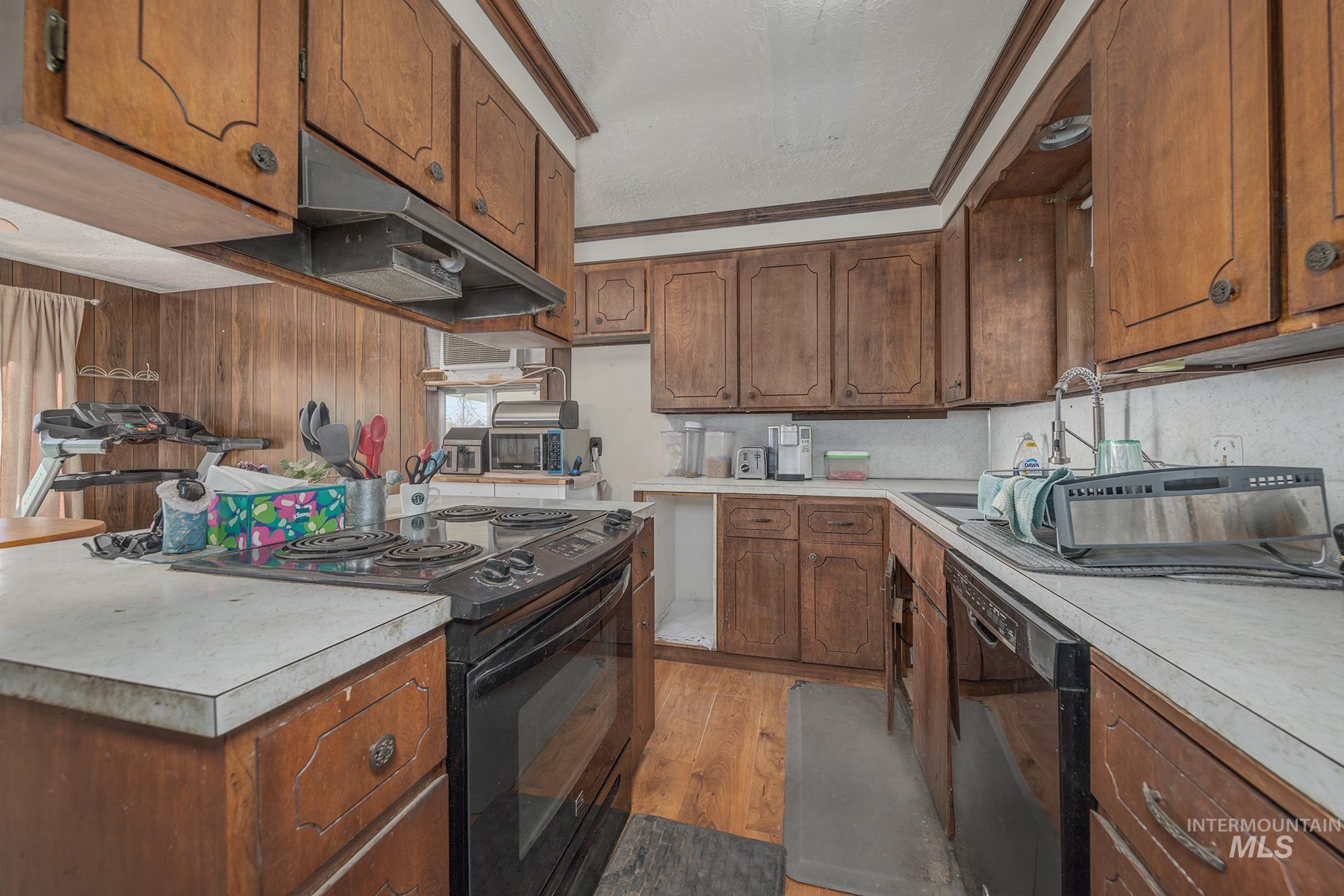 Kitchen with black appliances, wood finish cabinetry, light countertops, and light wood-style flooring