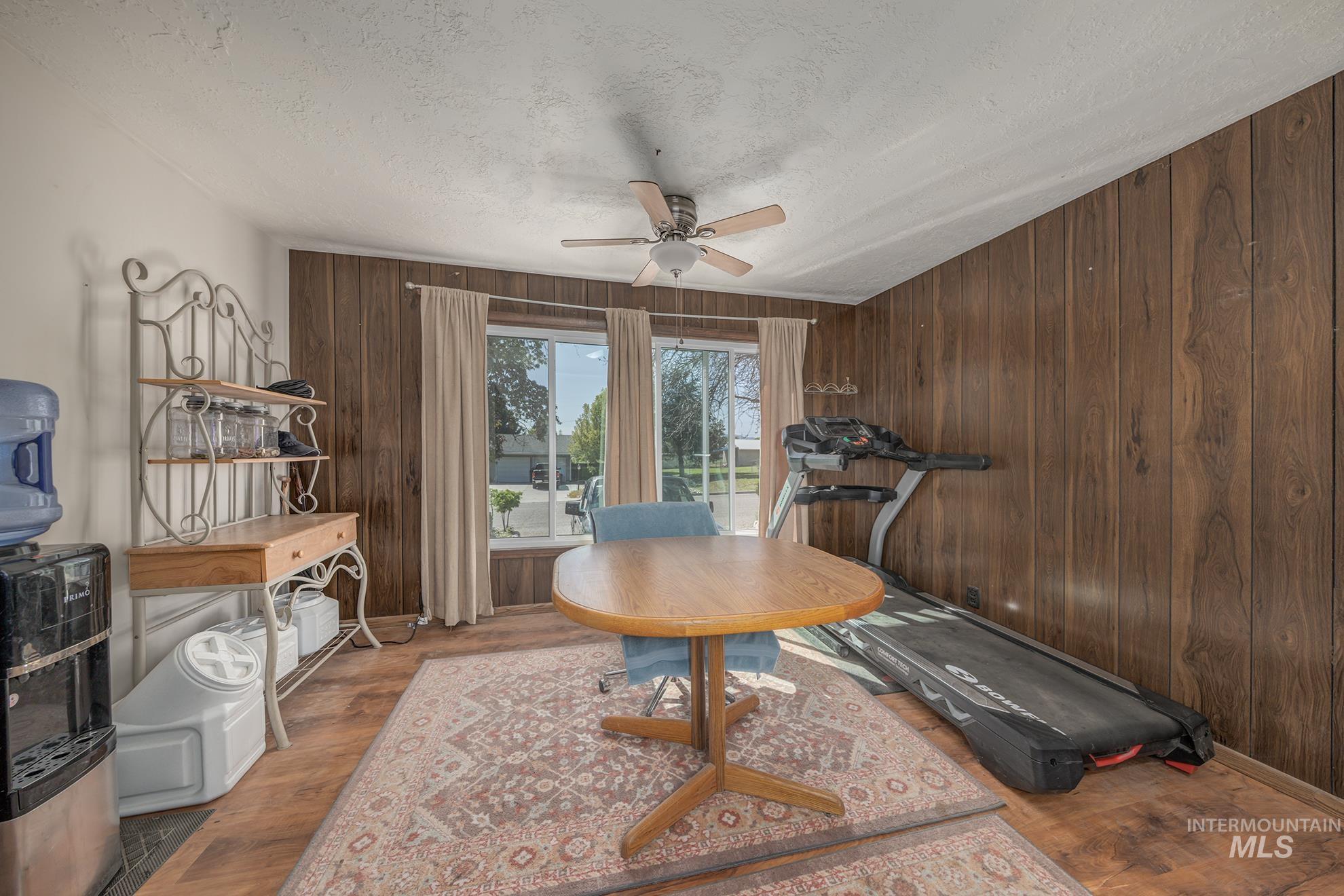 Home office with wood finished floors, a ceiling fan, wooden walls, and a textured ceiling
