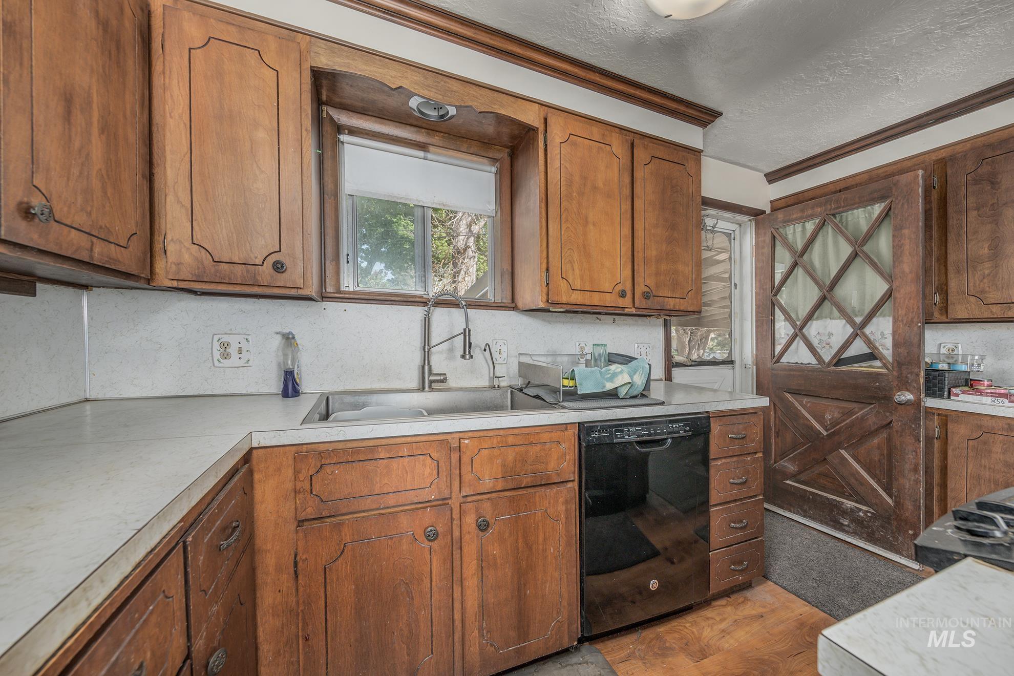 Kitchen with dishwasher, wood finish cabinetry, light countertops, a textured ceiling, and crown molding