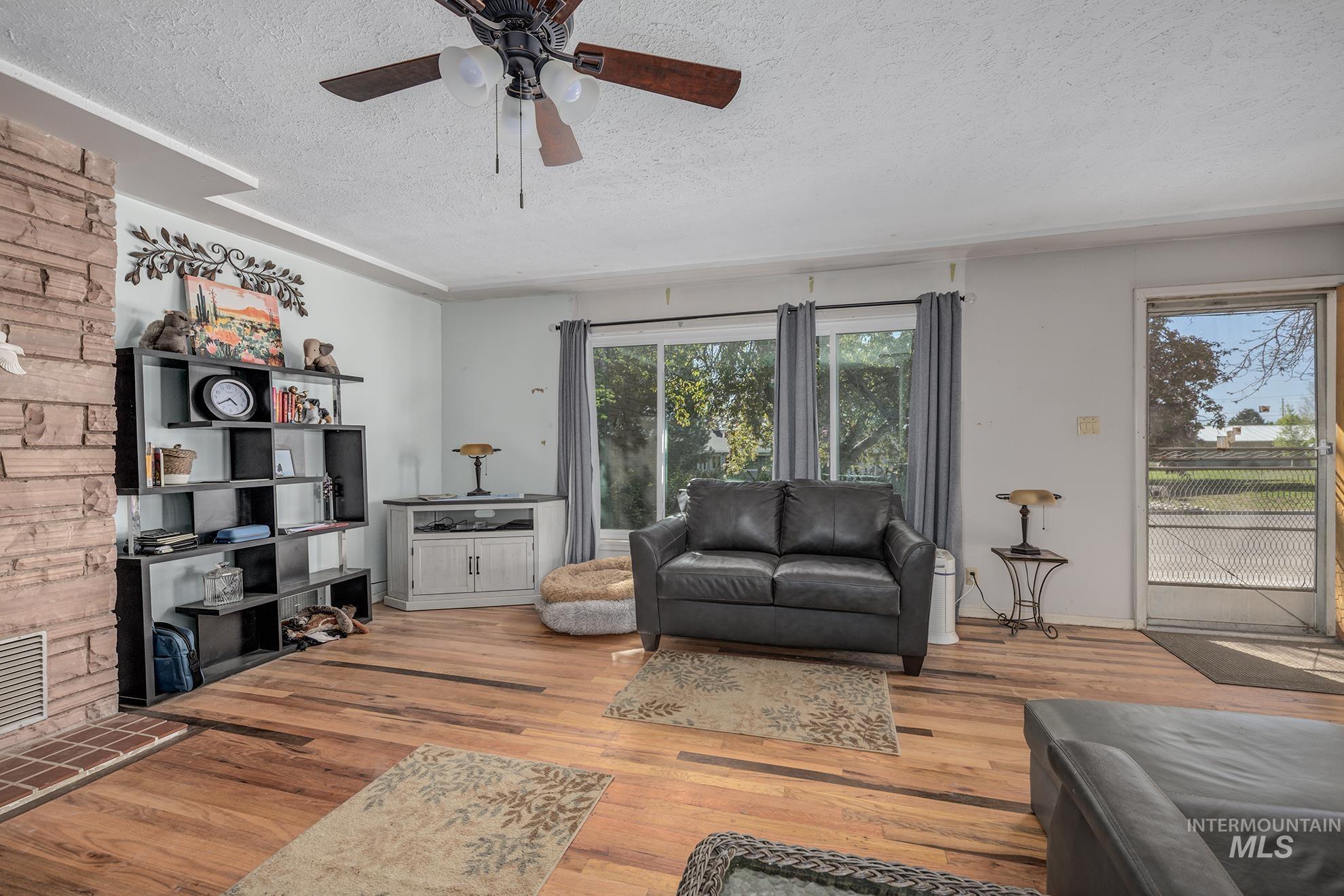 Living room with a textured ceiling, light wood-style floors, and ceiling fan