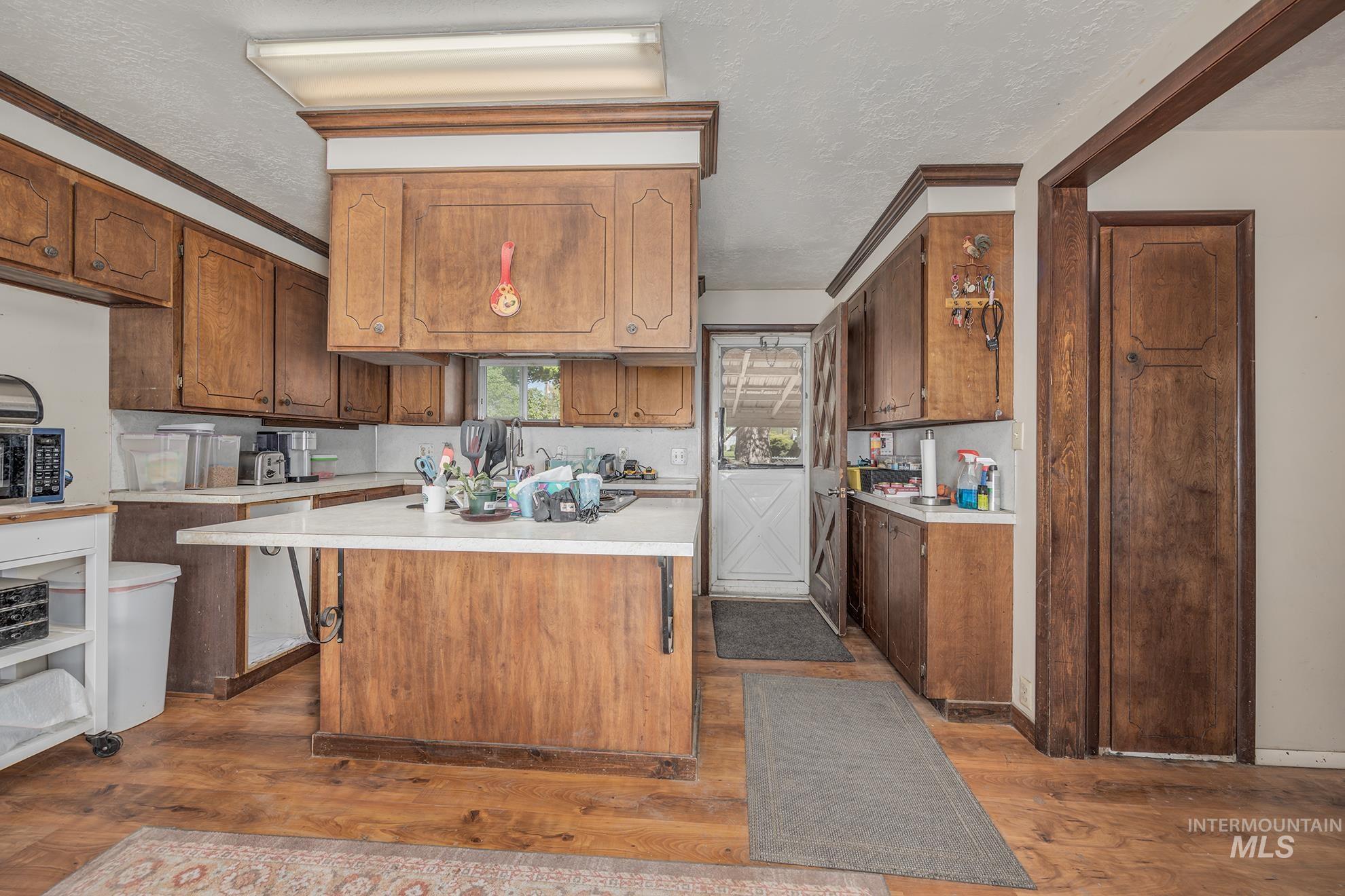 Kitchen with light countertops, a center island, dark wood-type flooring, a textured ceiling, and wood finish cabinets