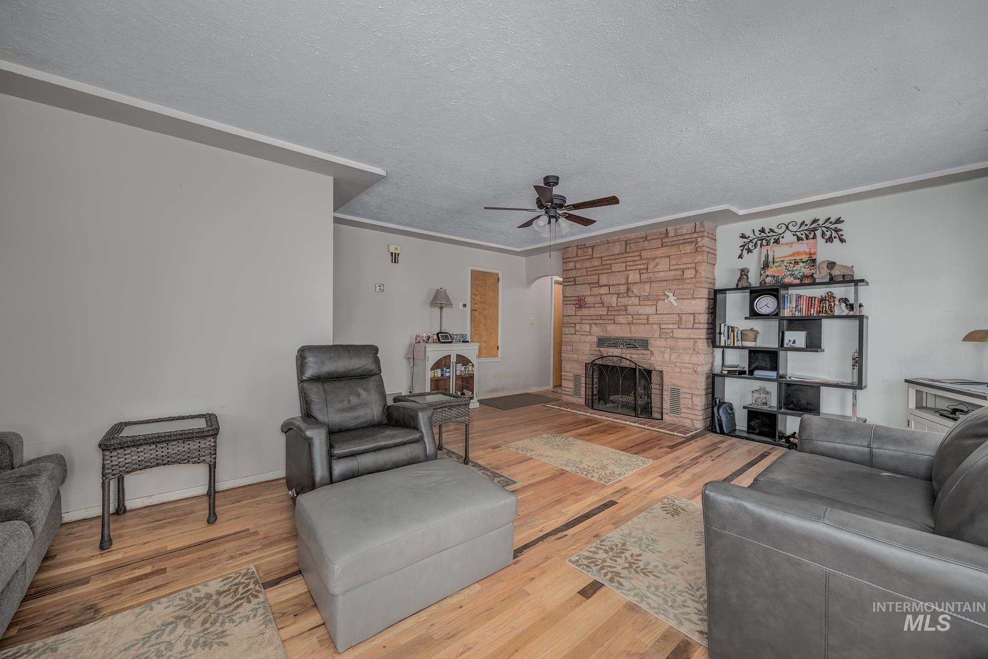 Living room featuring a fireplace, light wood-style floors, a ceiling fan, a textured ceiling, and ornamental molding