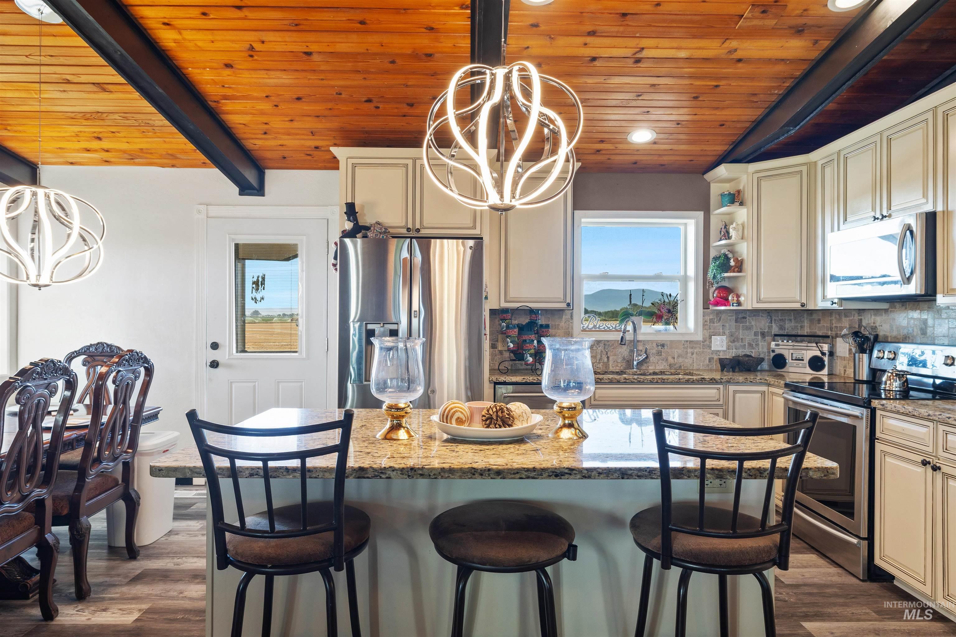 Kitchen with a chandelier, decorative light fixtures, appliances with stainless steel finishes, a wood ceiling with exposed beams, and a kitchen bar