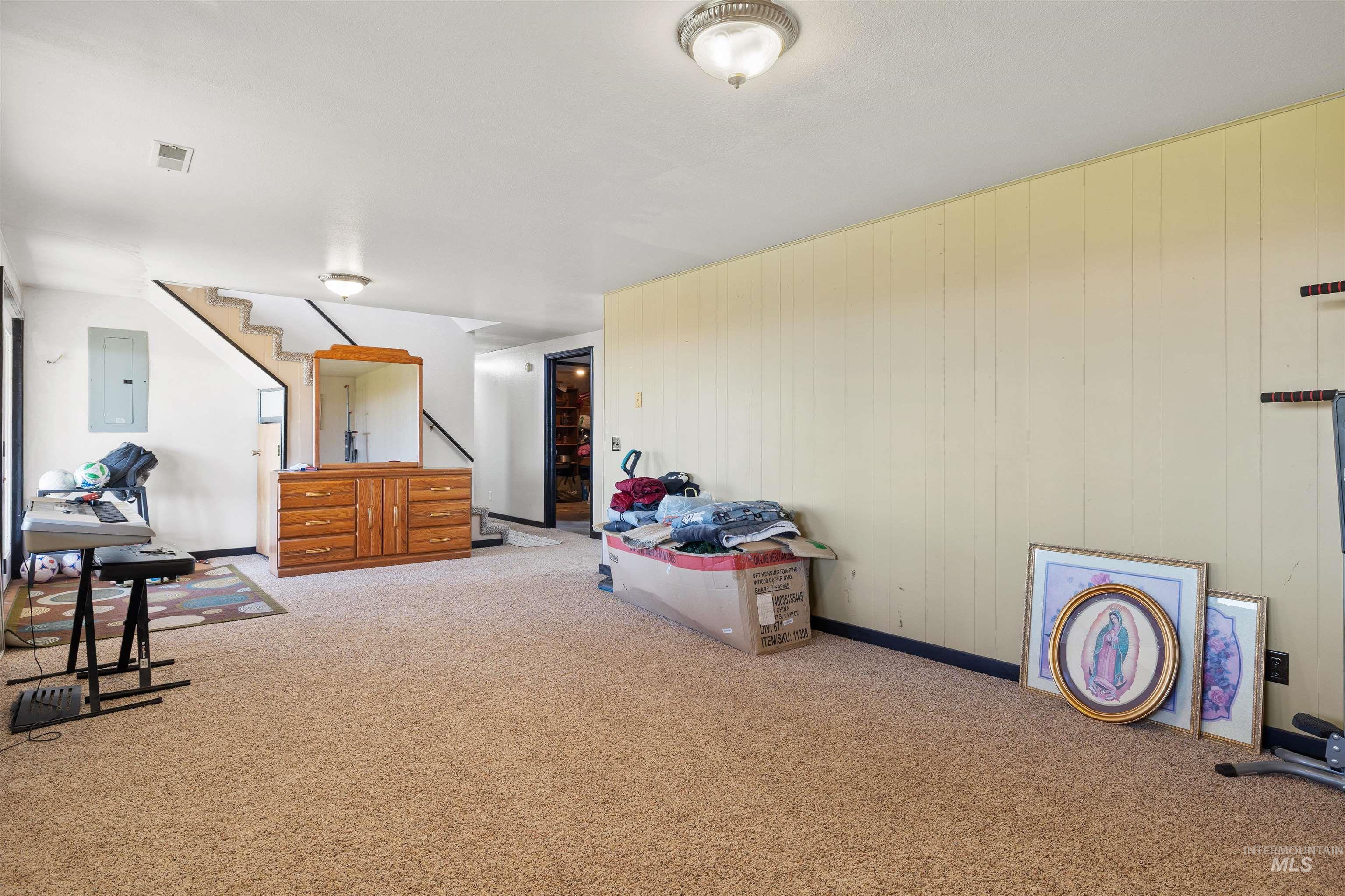 Sitting room featuring carpet, electric panel, wooden walls, and stairs