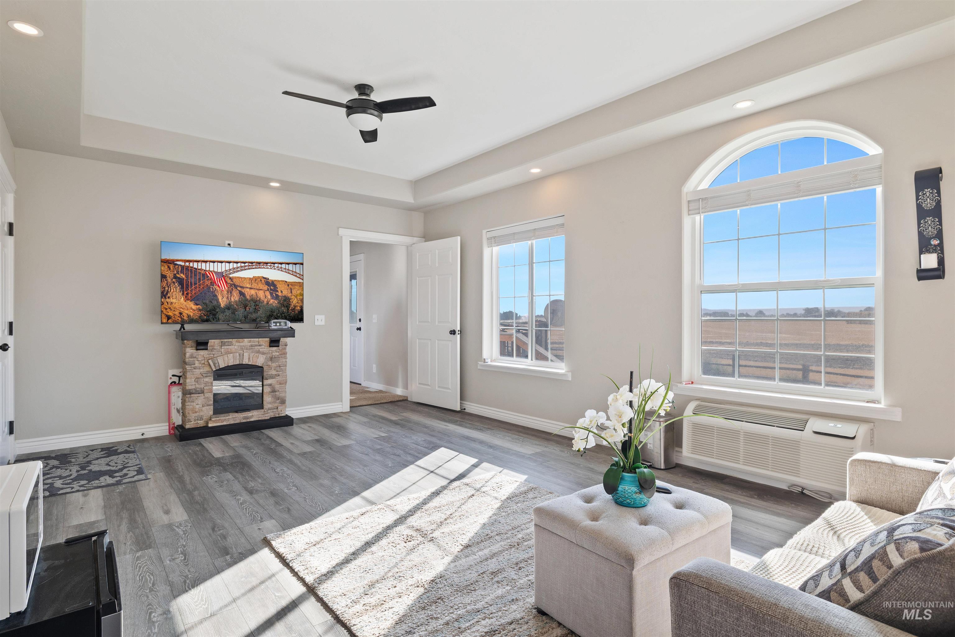 Living room with recessed lighting, ceiling fan, a tray ceiling, wood finished floors, and a fireplace