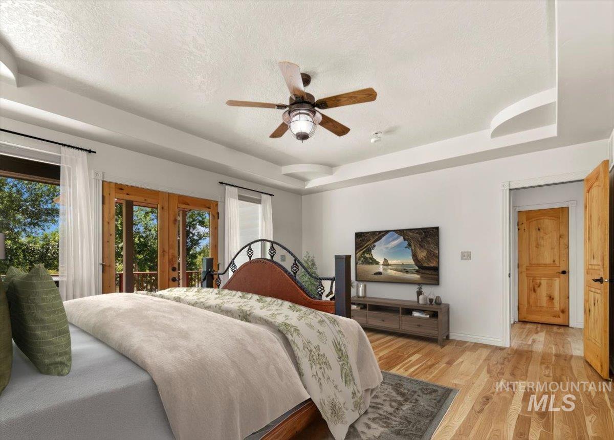 Bedroom with access to exterior, a textured ceiling, light wood-style flooring, a tray ceiling, and a ceiling fan