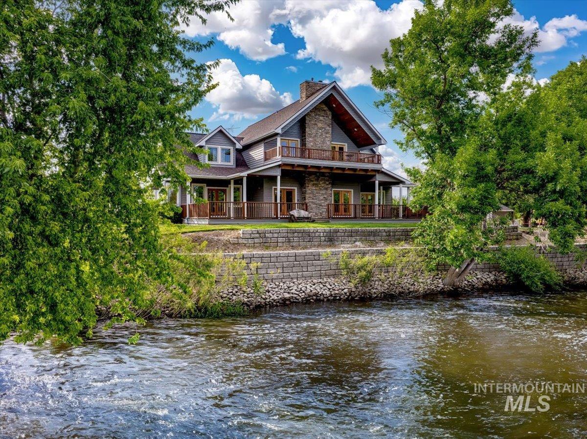 Rear view of house with a chimney, stone siding, a water view, and a balcony