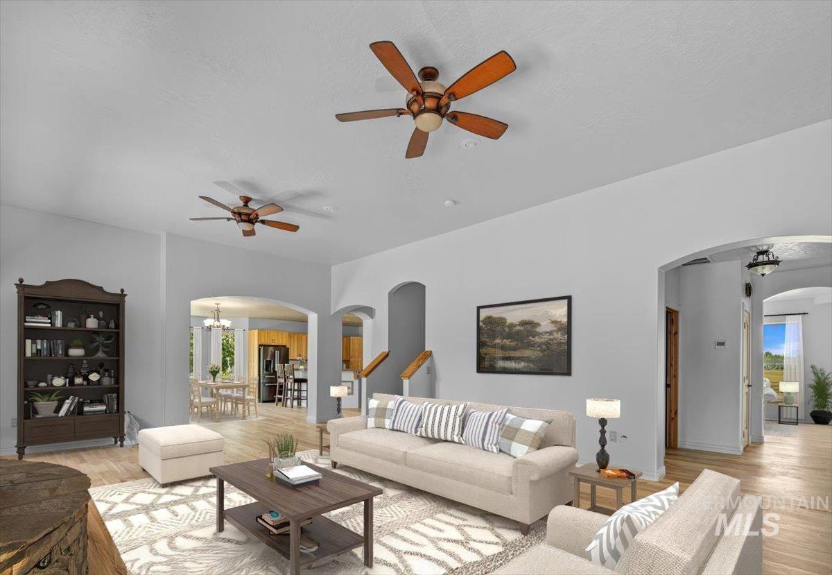 Living room with arched walkways, a ceiling fan, light wood-style floors, and a chandelier