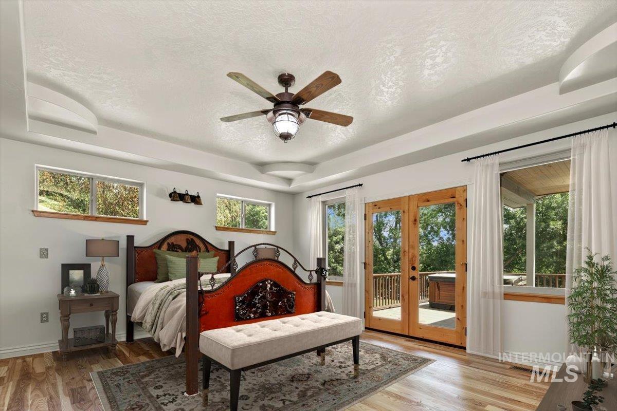 Bedroom featuring a tray ceiling, a textured ceiling, access to exterior, light wood-style floors, and french doors