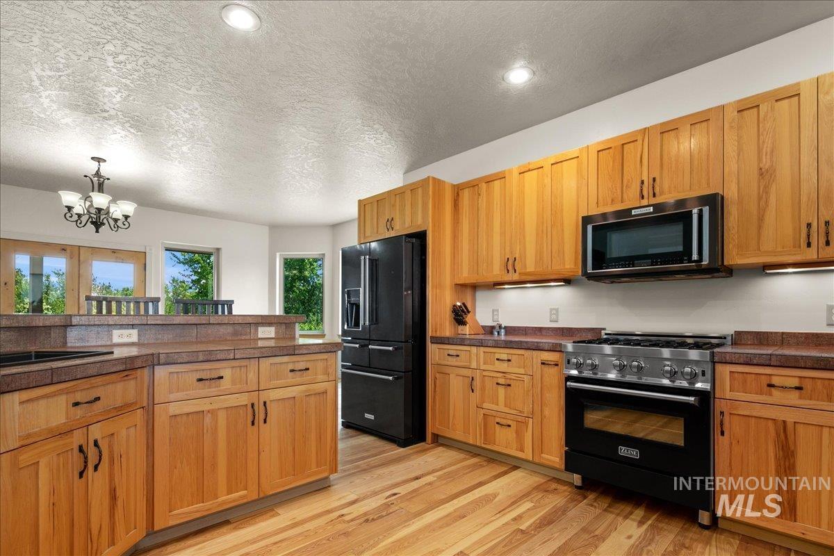 Kitchen featuring black appliances, tile countertops, light wood finished floors, a chandelier, and a textured ceiling