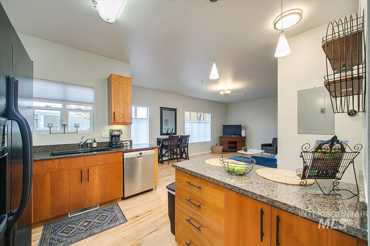 Kitchen featuring stainless steel dishwasher, electric panel, light wood finished floors, brown cabinetry, and dark stone counters