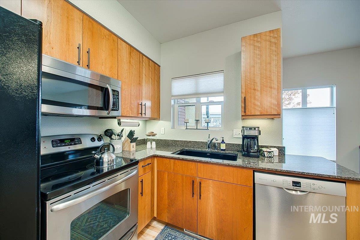 Kitchen featuring appliances with stainless steel finishes, dark stone countertops, healthy amount of natural light, and brown cabinetry