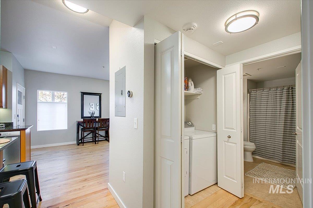 Laundry area featuring electric panel, light wood-style flooring, and washing machine and clothes dryer