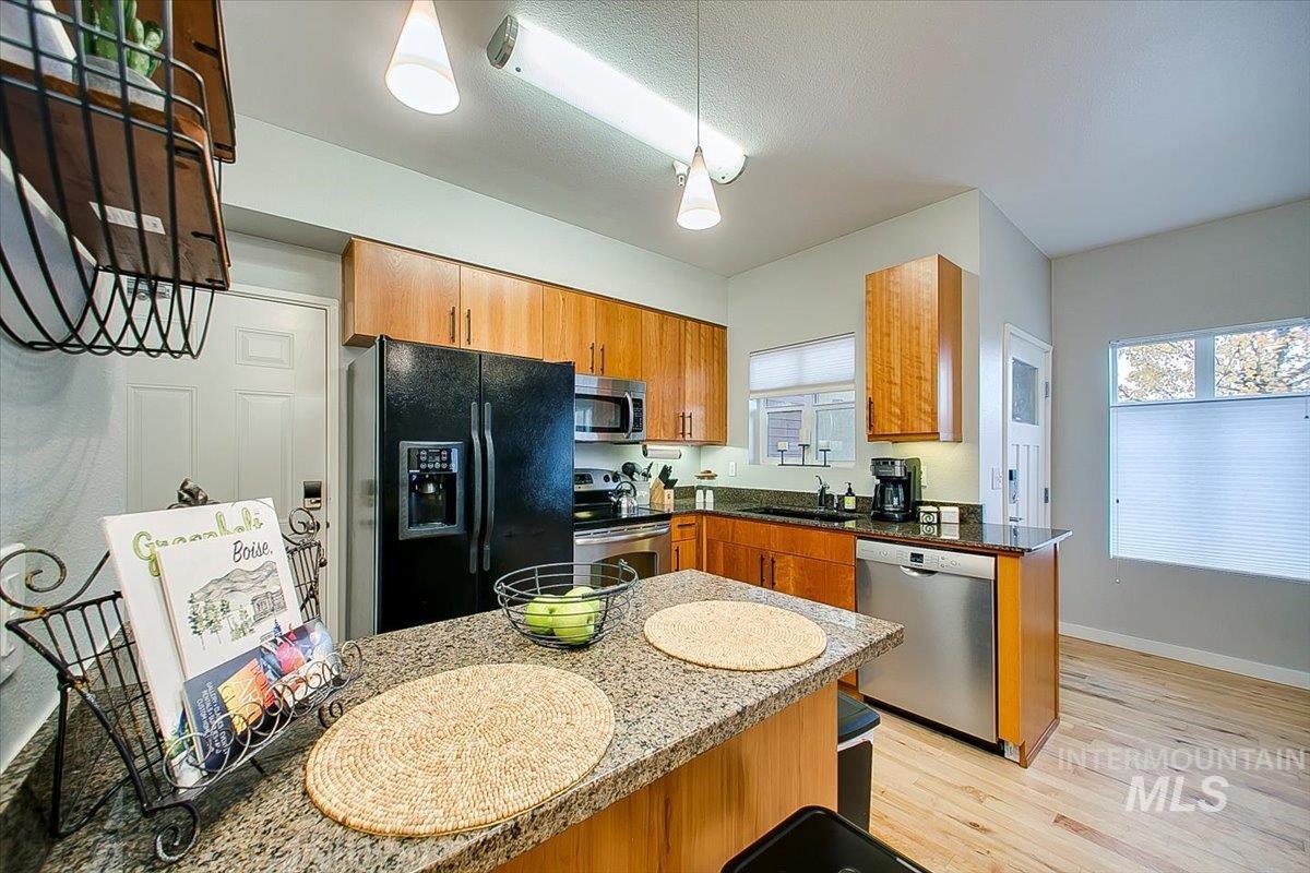 Kitchen with stainless steel appliances, light wood finished floors, brown cabinetry, and hanging light fixtures