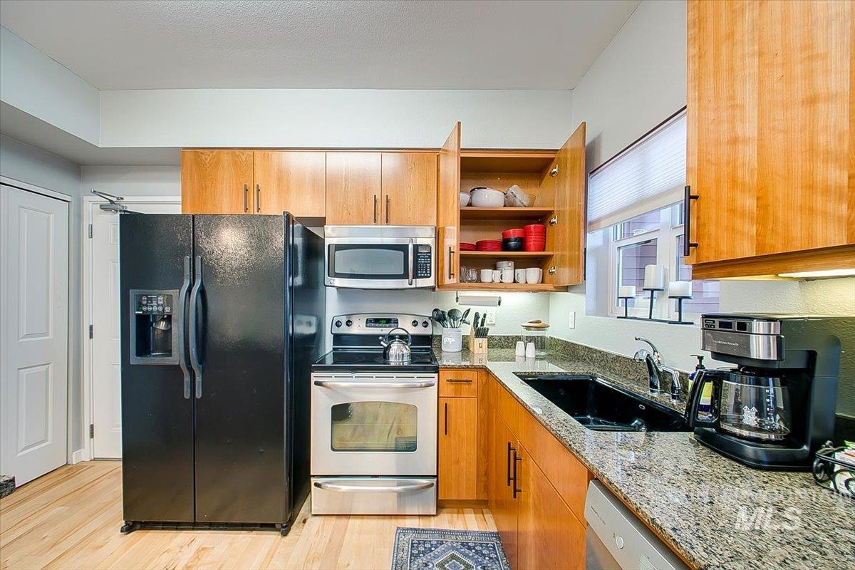 Kitchen featuring stainless steel appliances, light stone countertops, light wood-type flooring, brown cabinetry, and open shelves
