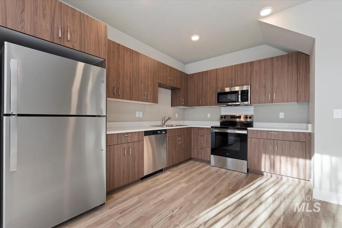 Kitchen with stainless steel appliances, modern cabinets, light wood finished floors, recessed lighting, and brown cabinetry