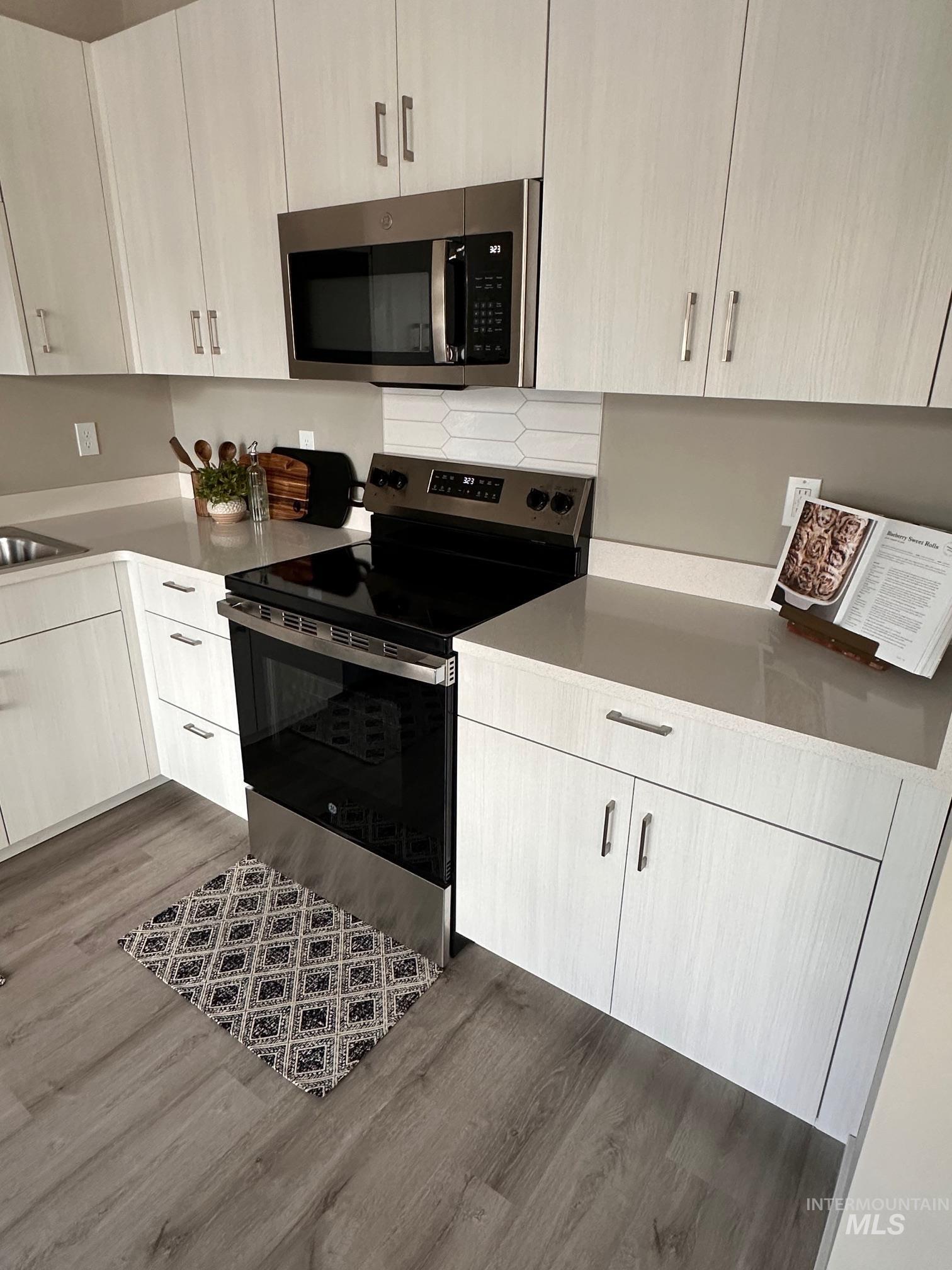 Kitchen with appliances with stainless steel finishes, dark wood-style floors, light stone counters, and decorative backsplash