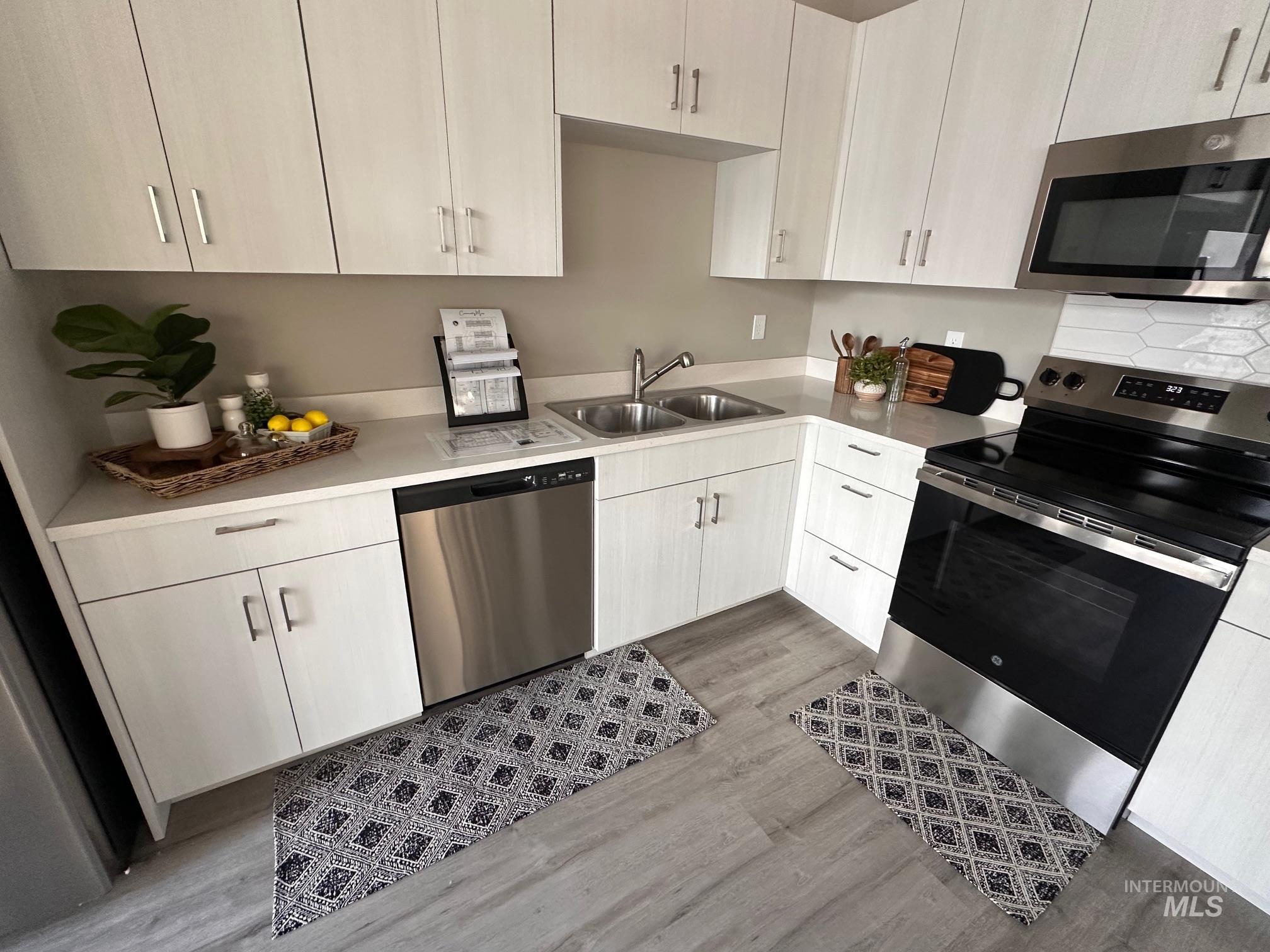 Kitchen featuring appliances with stainless steel finishes, light wood-style flooring, white cabinets, and light countertops