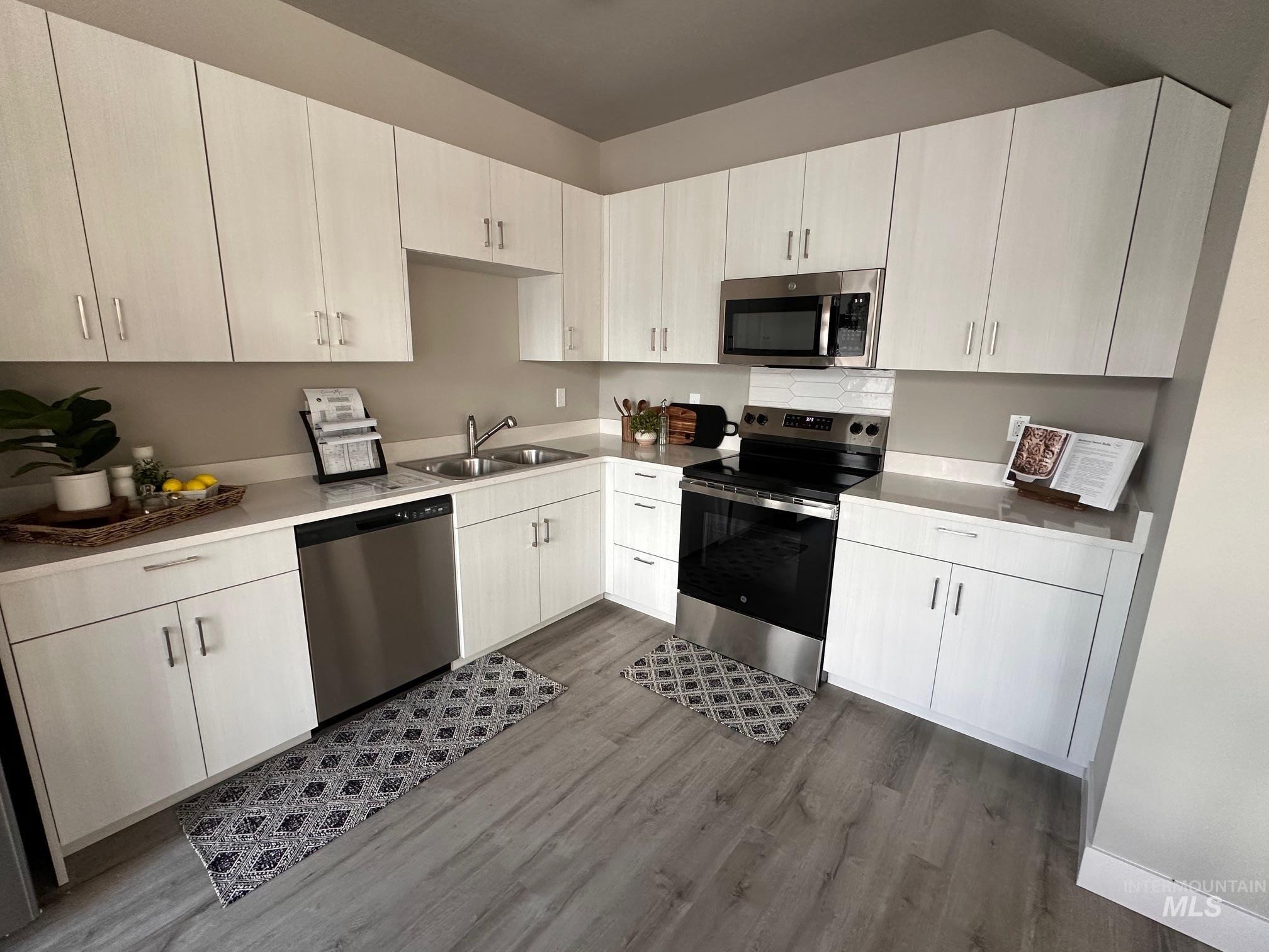 Kitchen with appliances with stainless steel finishes, white cabinets, dark wood-style floors, and light countertops