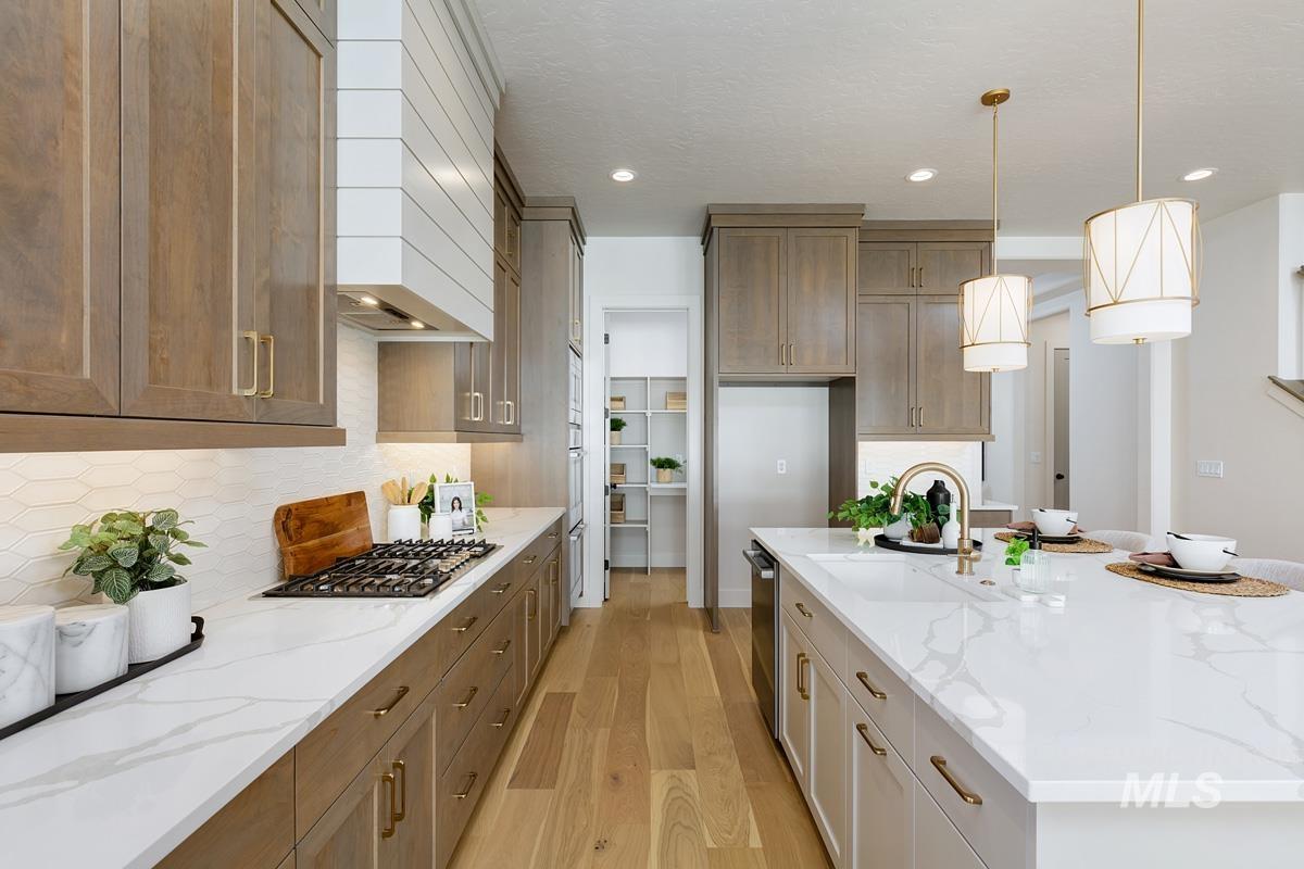 Kitchen with light stone counters, pendant lighting, light wood finished floors, a large island with sink, and premium range hood
