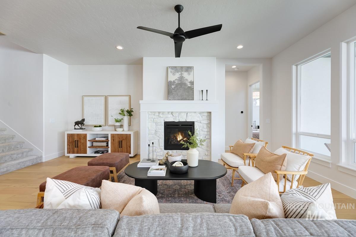 Living area with light wood finished floors, a stone fireplace, recessed lighting, stairway, and a ceiling fan