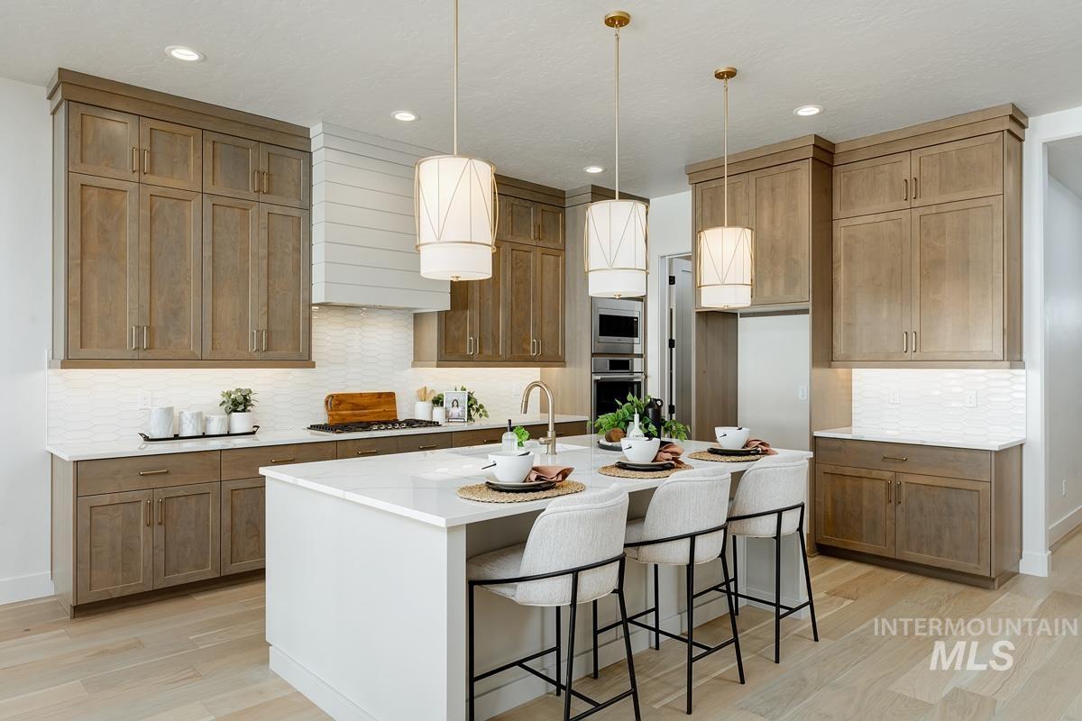 Kitchen featuring decorative backsplash, a kitchen bar, hanging light fixtures, light stone counters, and brown cabinetry