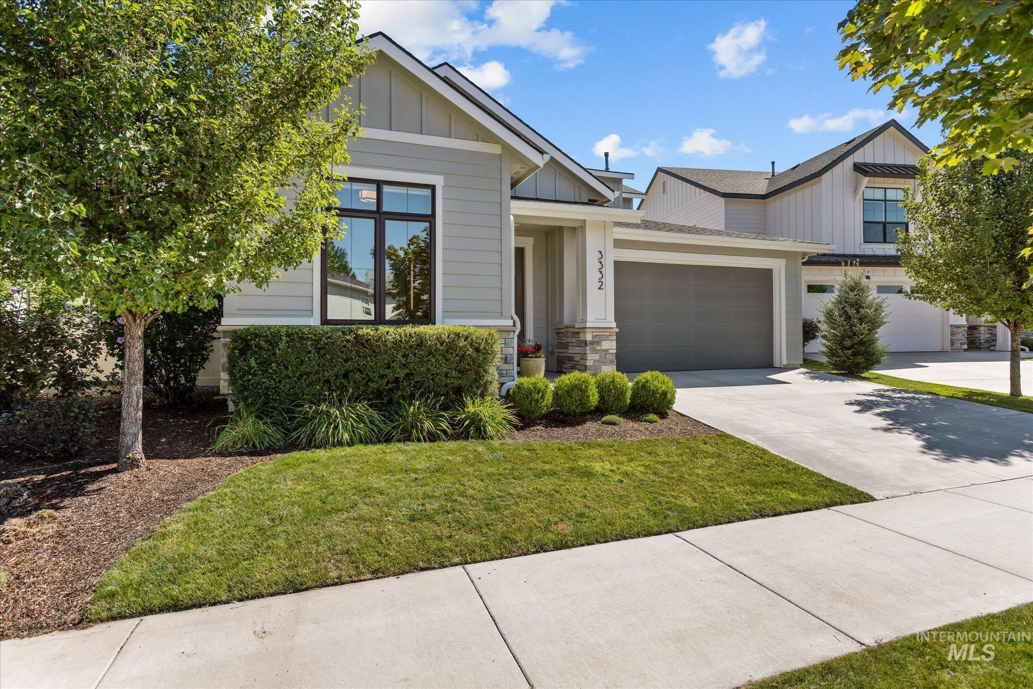 View of front of property with board and batten siding, driveway, stone siding, a front yard, and an attached garage