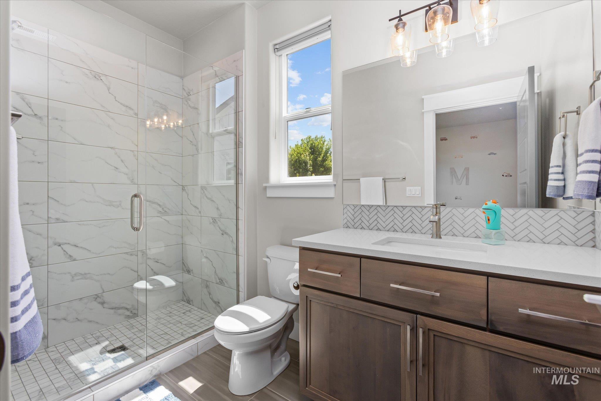 Bathroom featuring vanity, a chandelier, a stall shower, wood finished floors, and backsplash