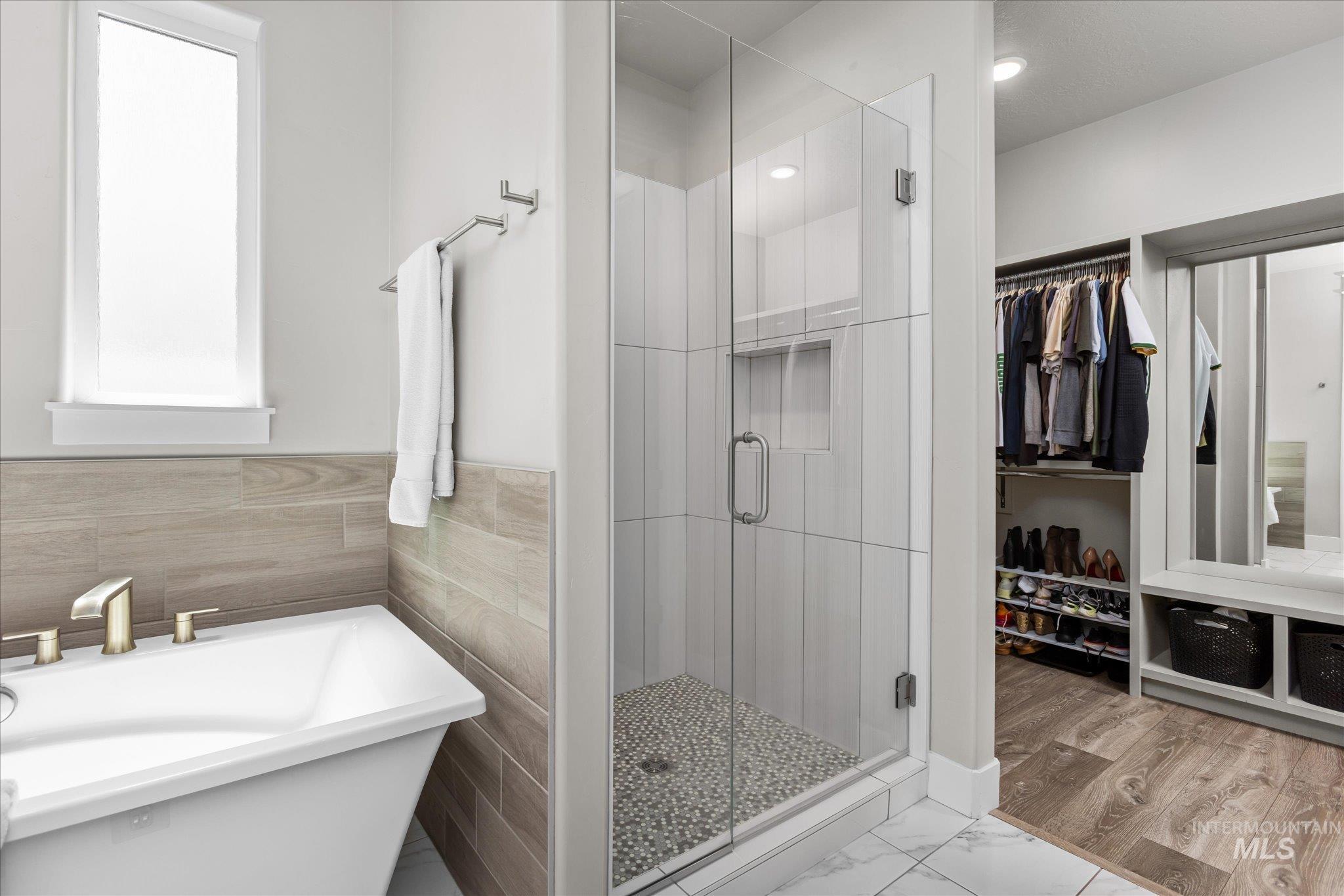 Bathroom with a stall shower, a walk in closet, a freestanding tub, and marble look tiles